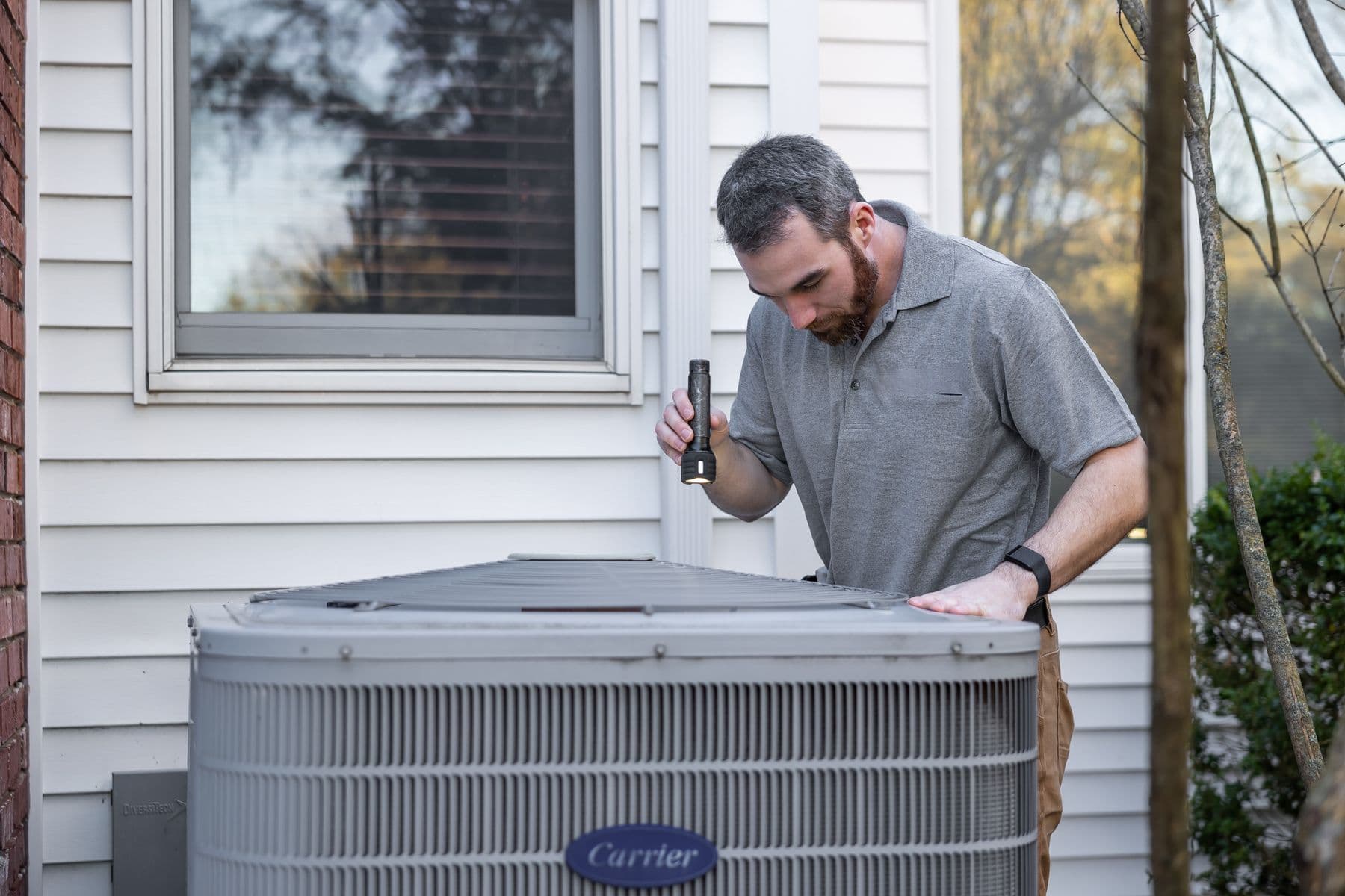 Technician inspecting an outdoor air conditioning unit beside a home