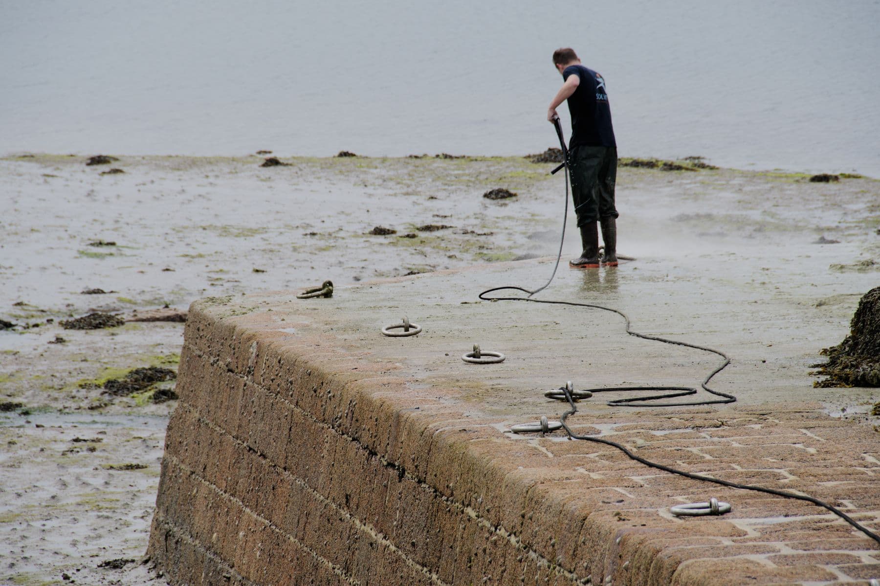 Worker pressure washing a stone pier beside the water