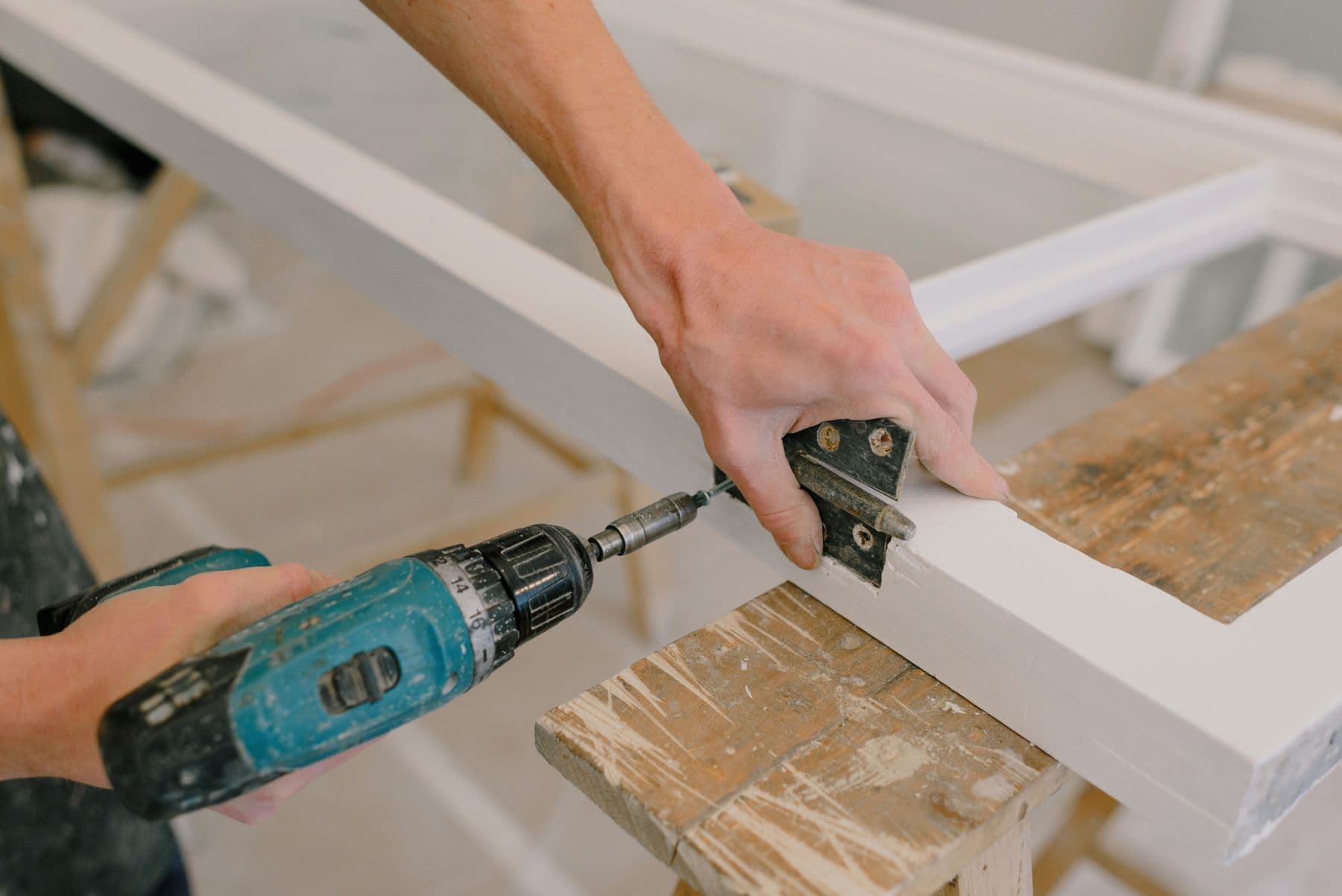 Craftsperson using a cordless drill to fasten a hinge to a wooden frame