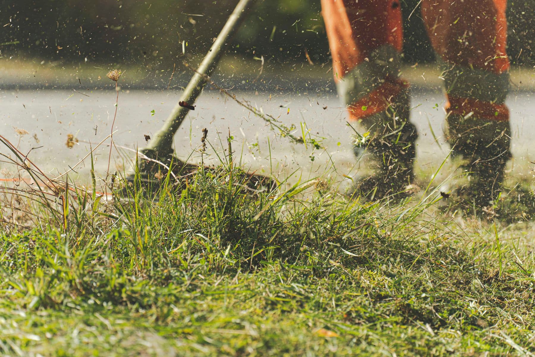 Worker using a string trimmer to cut grass in natural sunlight