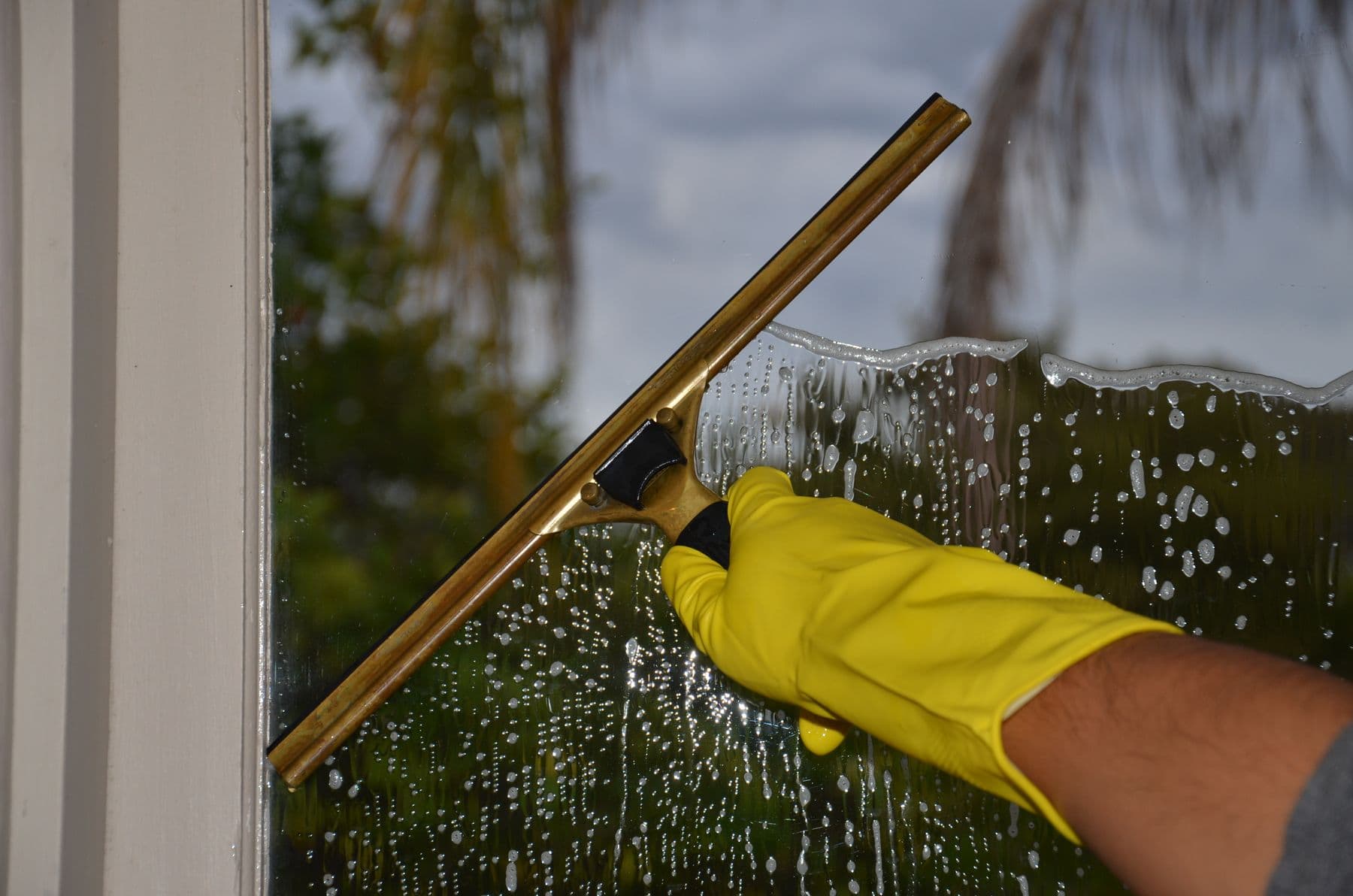 Gloved hand using a squeegee to clean a glass window